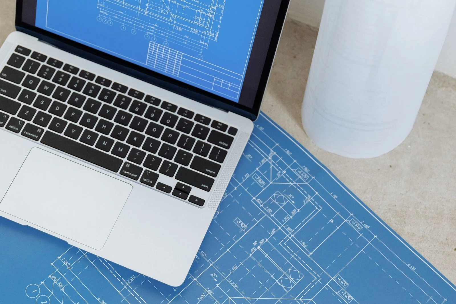 Projeto técnico aberto ao lado de um notebook, representando a redação do relatório descritivo e das reivindicações de uma patente