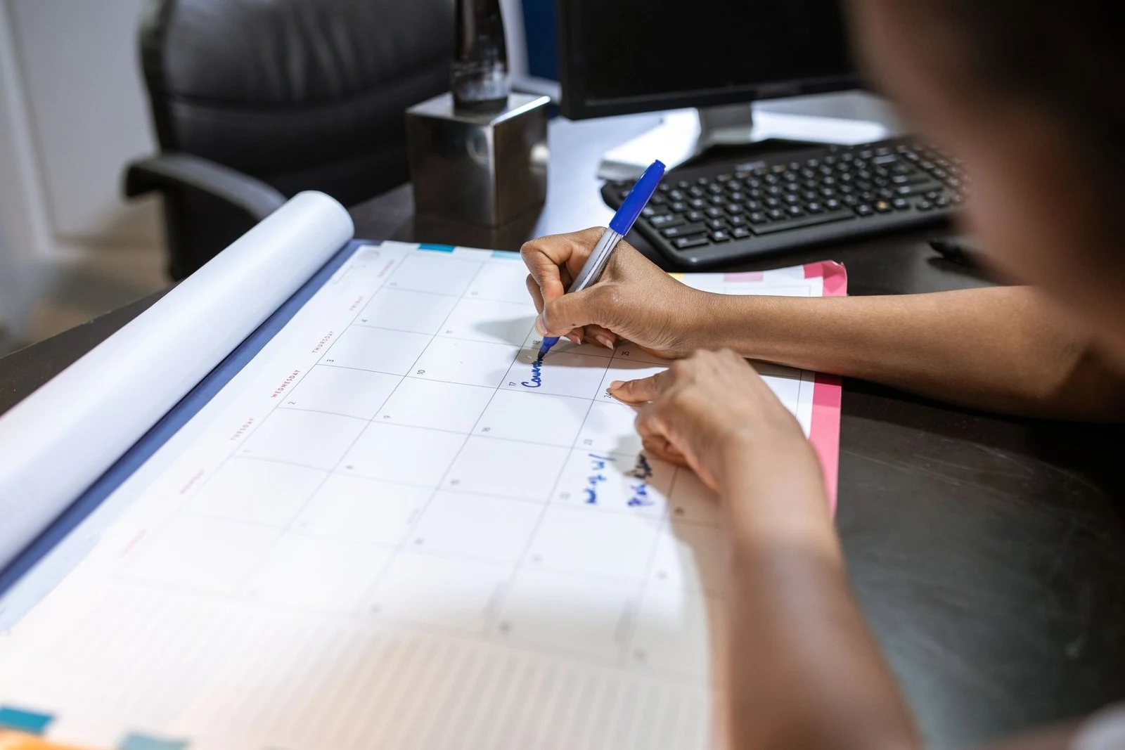 Profissional anotando datas em calendário de mesa para controlar prazos internos